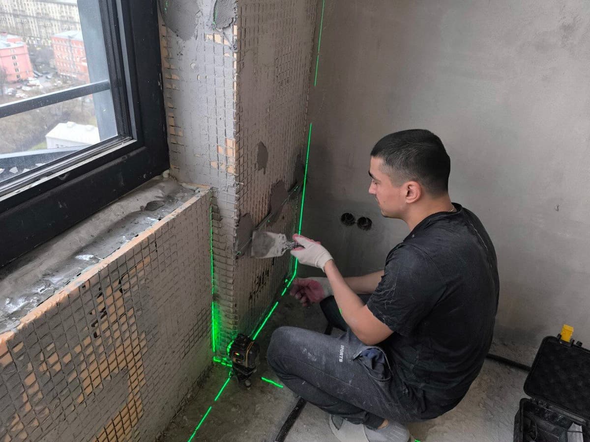 Мастер штукатурит оконные откосы с лазерным уровнем