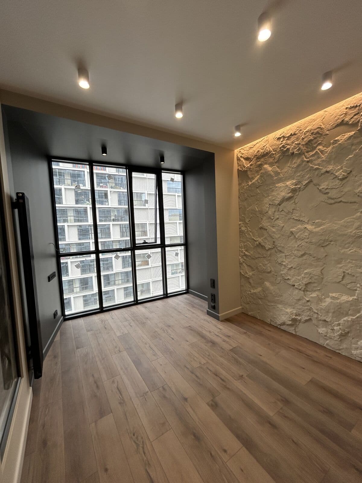 Гостиная — панорамное окно, декоративная стена «скала» с подсветкой, чёрный радиатор